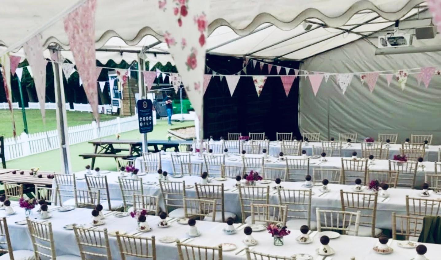 Long banquet tables laid for a cricket tea under the club marquee with bunting