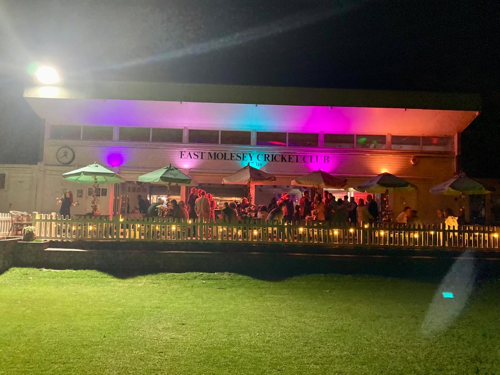 The pavilion lit in magenta and purple at night with guests on the terrace